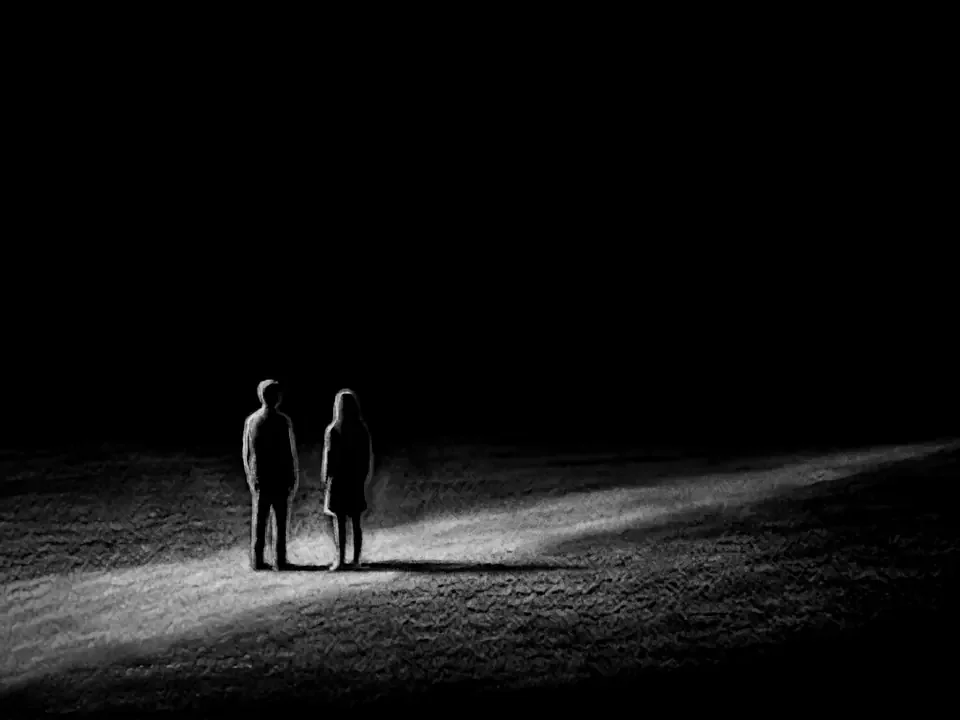 Two figures standing together in a pool of light in the dark